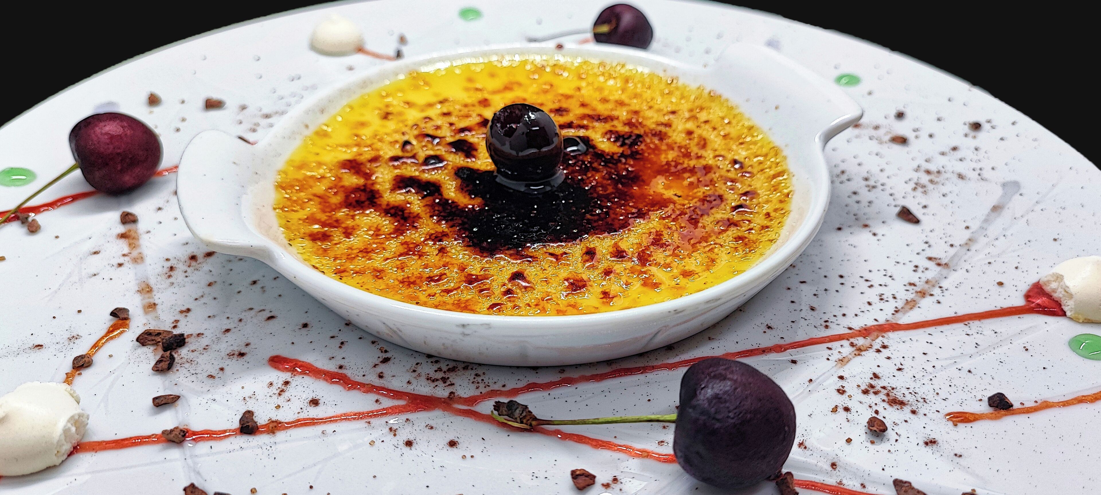 Un plato de postre con una cucharada de crema y una esfera de chocolate sobre una vajilla blanca con trozos de chocolate y frutas secas.