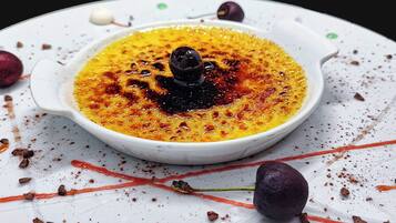 Un plato de postre con una cucharada de crema y una esfera de chocolate sobre una vajilla blanca con trozos de chocolate y frutas secas.