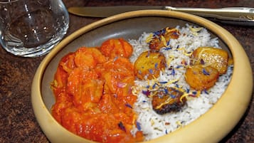 A bowl of food with rice and curry, a glass of water, and a spoon on a table.