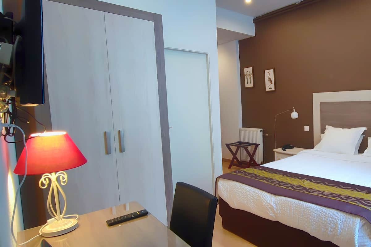 Une chambre d’hôtel comprenant un lit, des tables de chevet, un bureau avec une lampe, une chaise et une armoire.