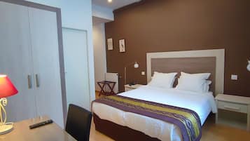 A hotel room with a bed, bedside tables, a desk with a lamp, a chair, and a wardrobe.