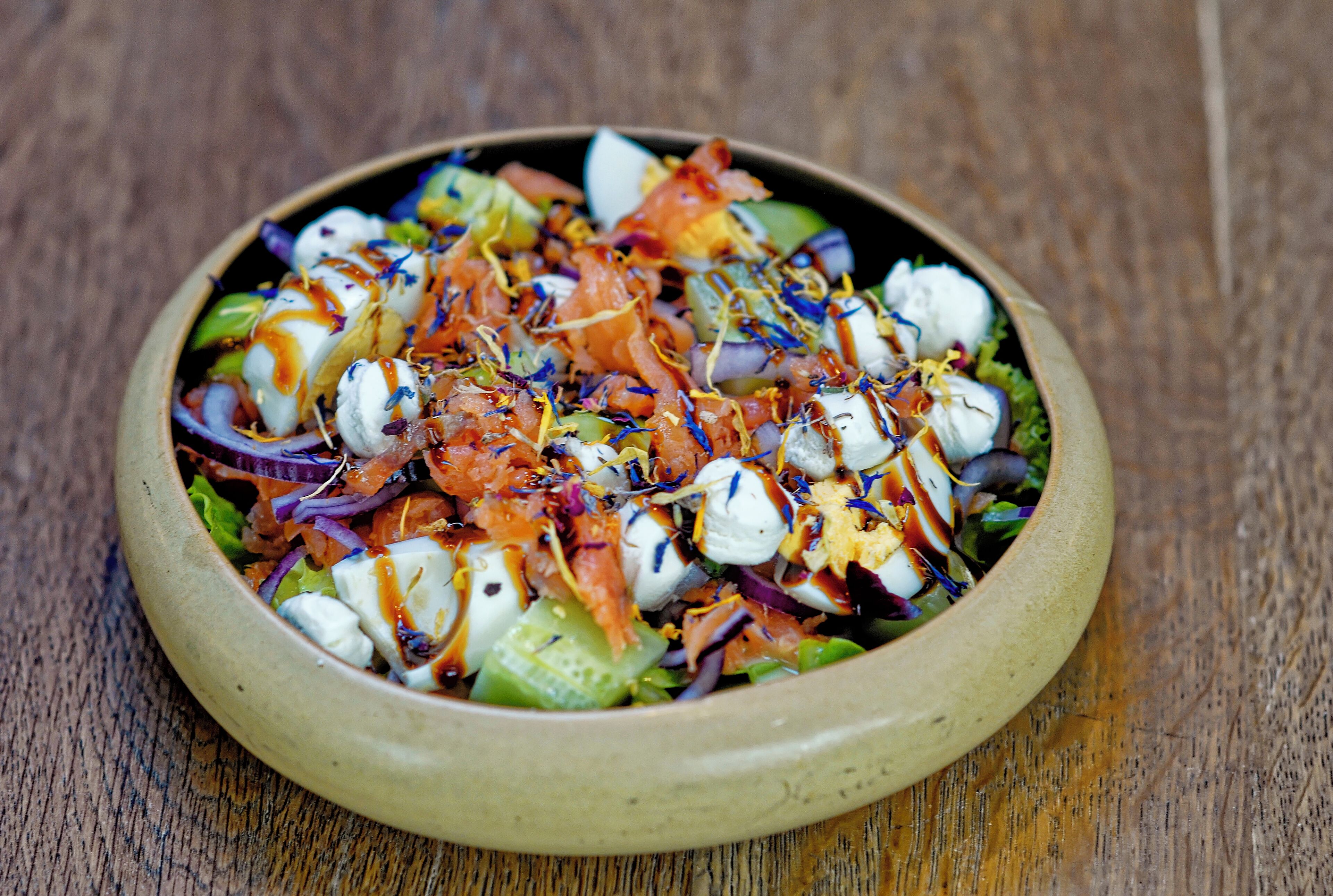 A bowl of salad with various ingredients and a drizzle of dressing.