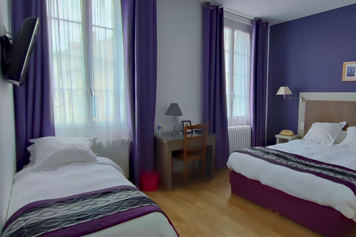 Une chambre d’hôtel avec deux lits, un bureau, une chaise et une fenêtre avec des rideaux violets.