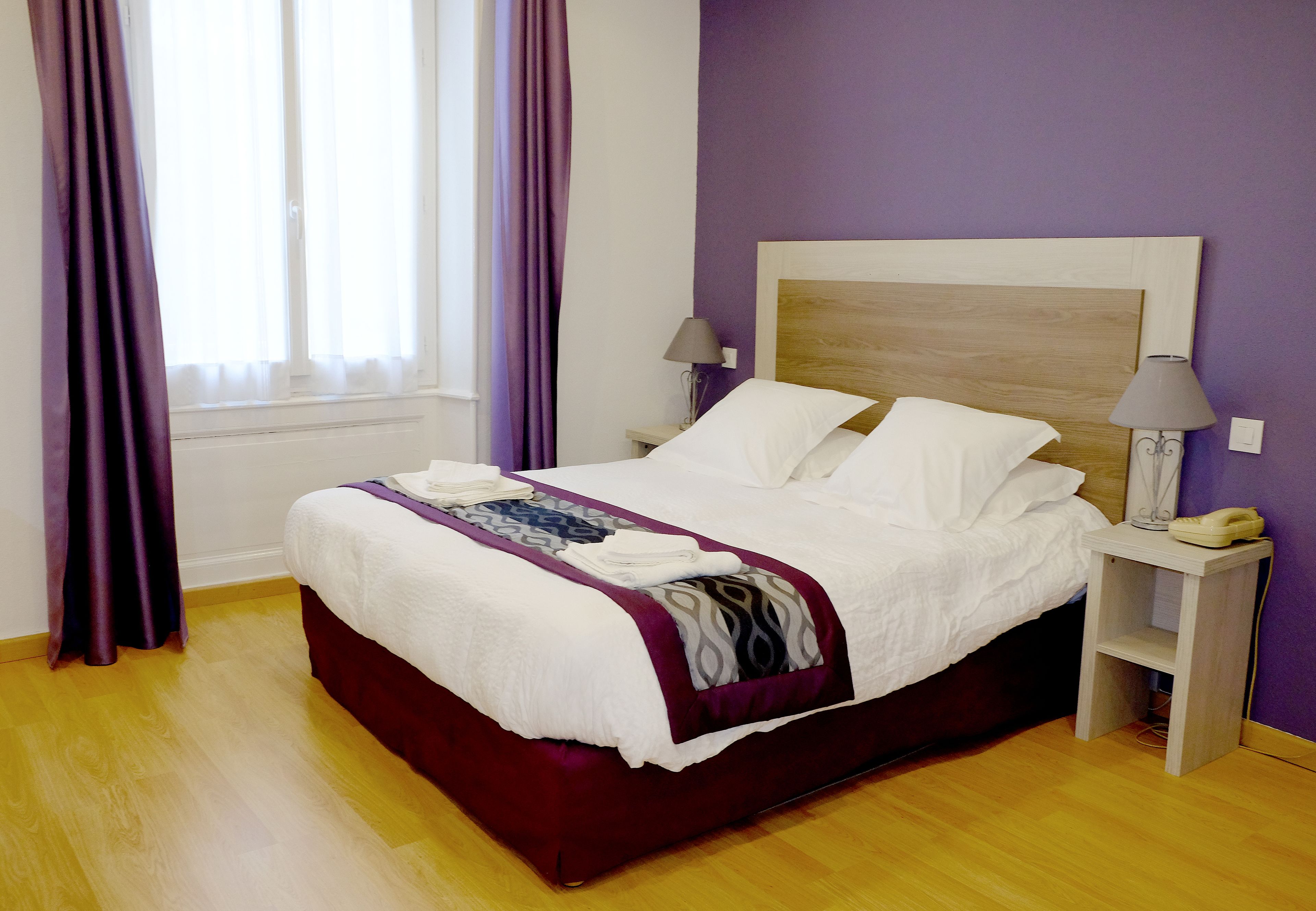 A neatly made bed with a wooden headboard, a bedside lamp, and a nightstand with a phone.
