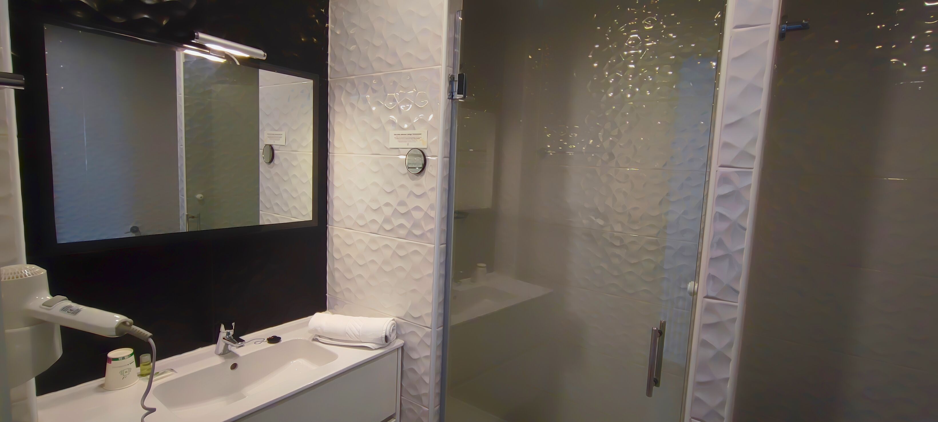 Un baño moderno con un espejo grande, un lavabo blanco y una zona de ducha con mampara de cristal.