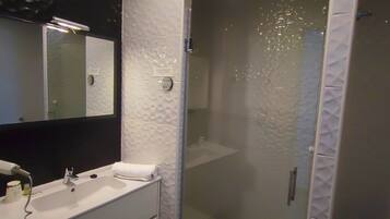 Un baño moderno con un espejo grande, un lavabo blanco y una zona de ducha con mampara de cristal.