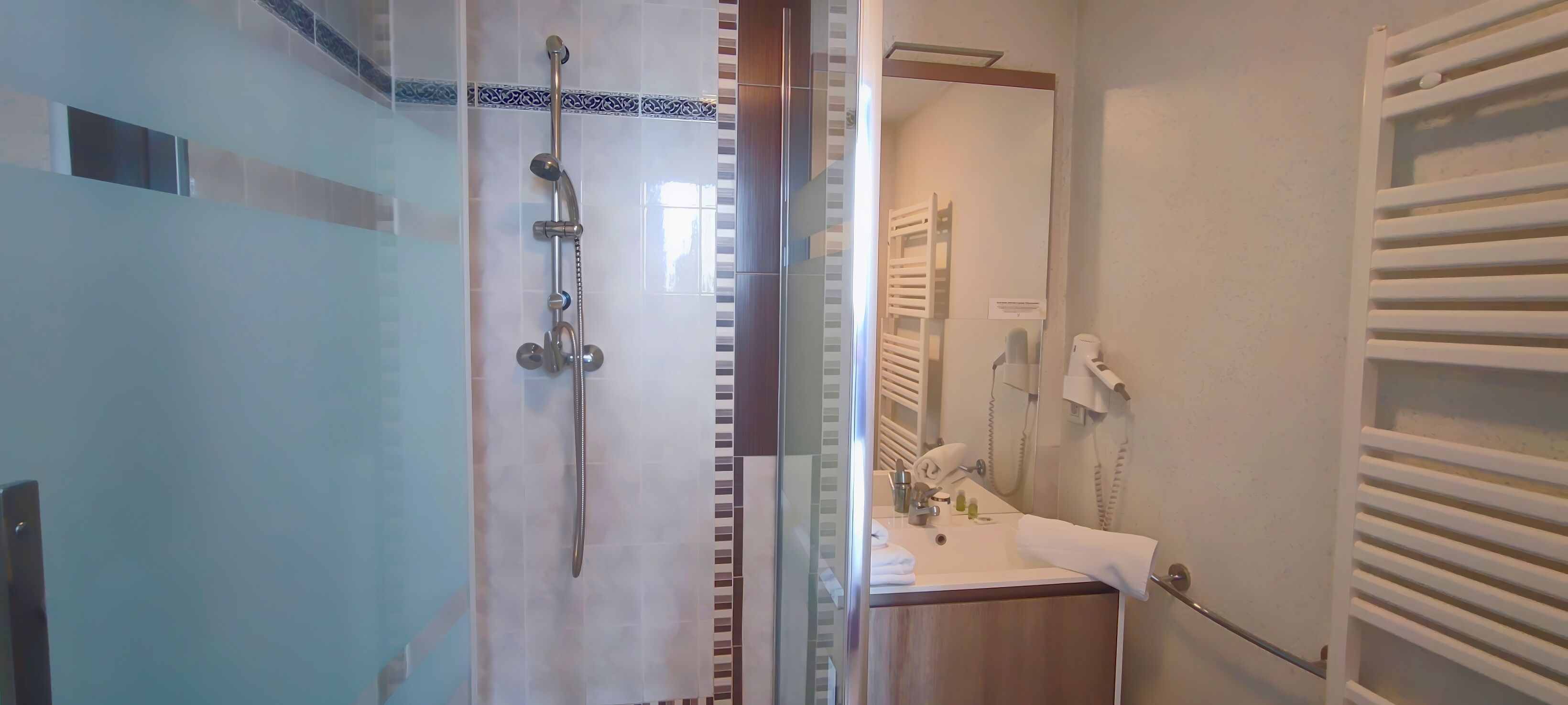 Une salle de bain moderne avec une douche à parois de verre, un lavabo blanc avec une serviette et un miroir.