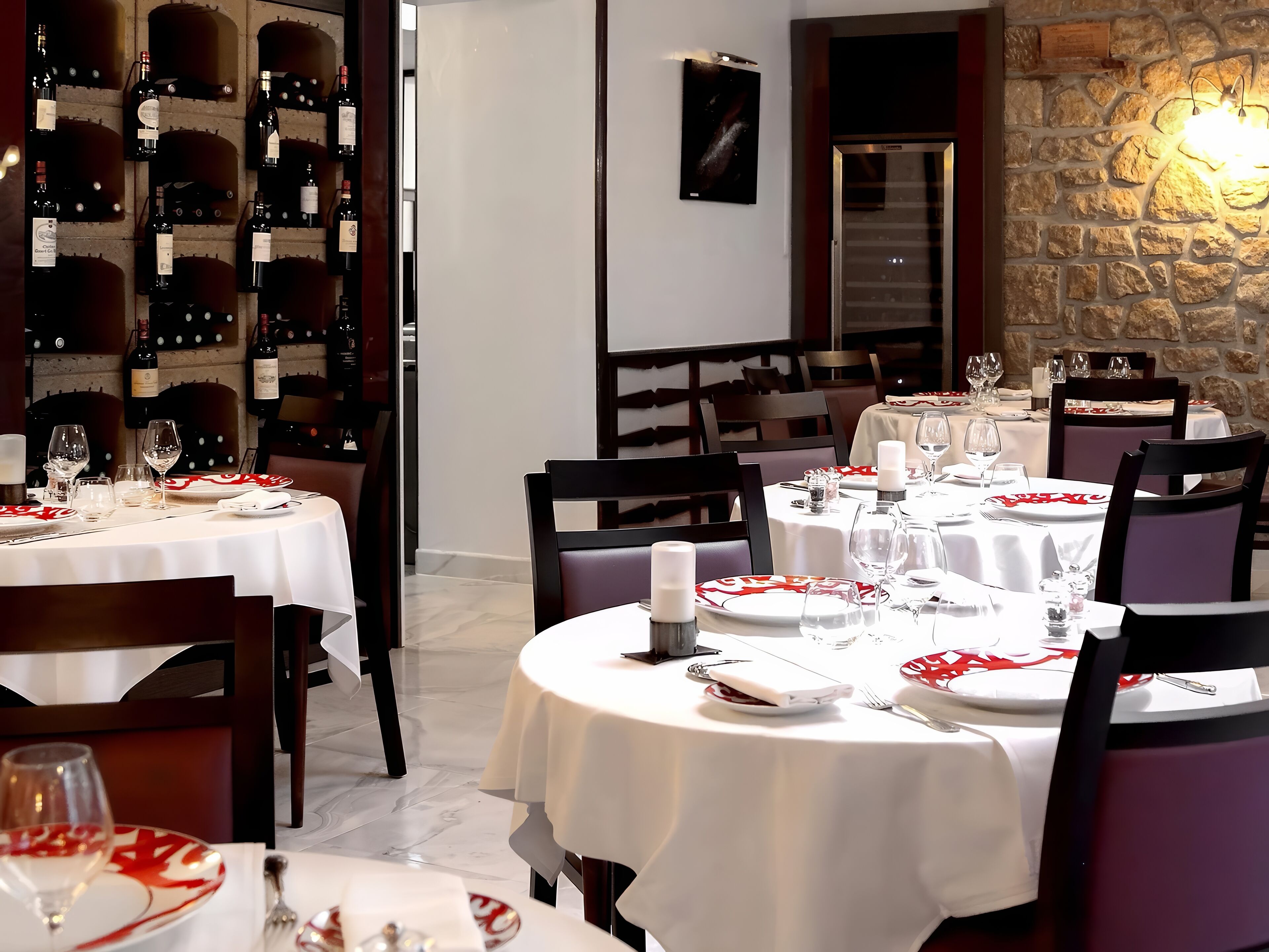 Un restaurant amb taules rodones preparades per sopar, amb tovallons blancs i plats amb dibuixos vermells i blancs.
