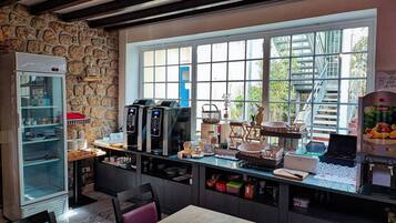 Une cuisine avec un mur en pierre, un réfrigérateur, une machine à café et une fenêtre donnant sur un paysage verdoyant.