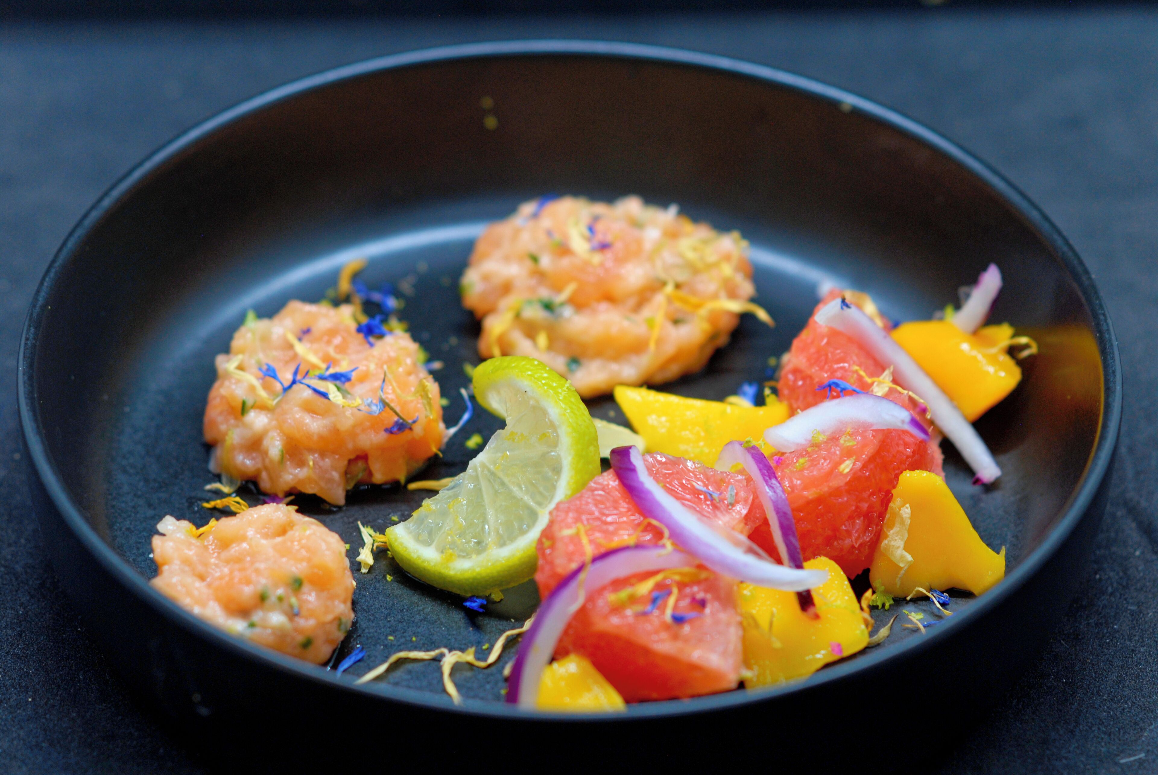 Un plato con camarones, lima y verduras coloridas sobre un fondo oscuro.
