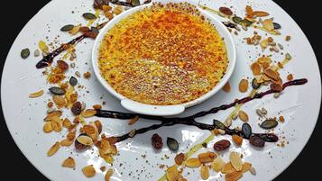 A dessert dish with a creamy topping, surrounded by various nuts and seeds on a white plate.
