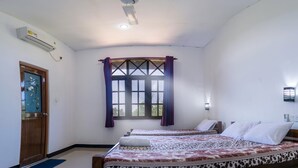A hotel room with two beds, a window with curtains, an air conditioning unit, and a wall-mounted light fixture.