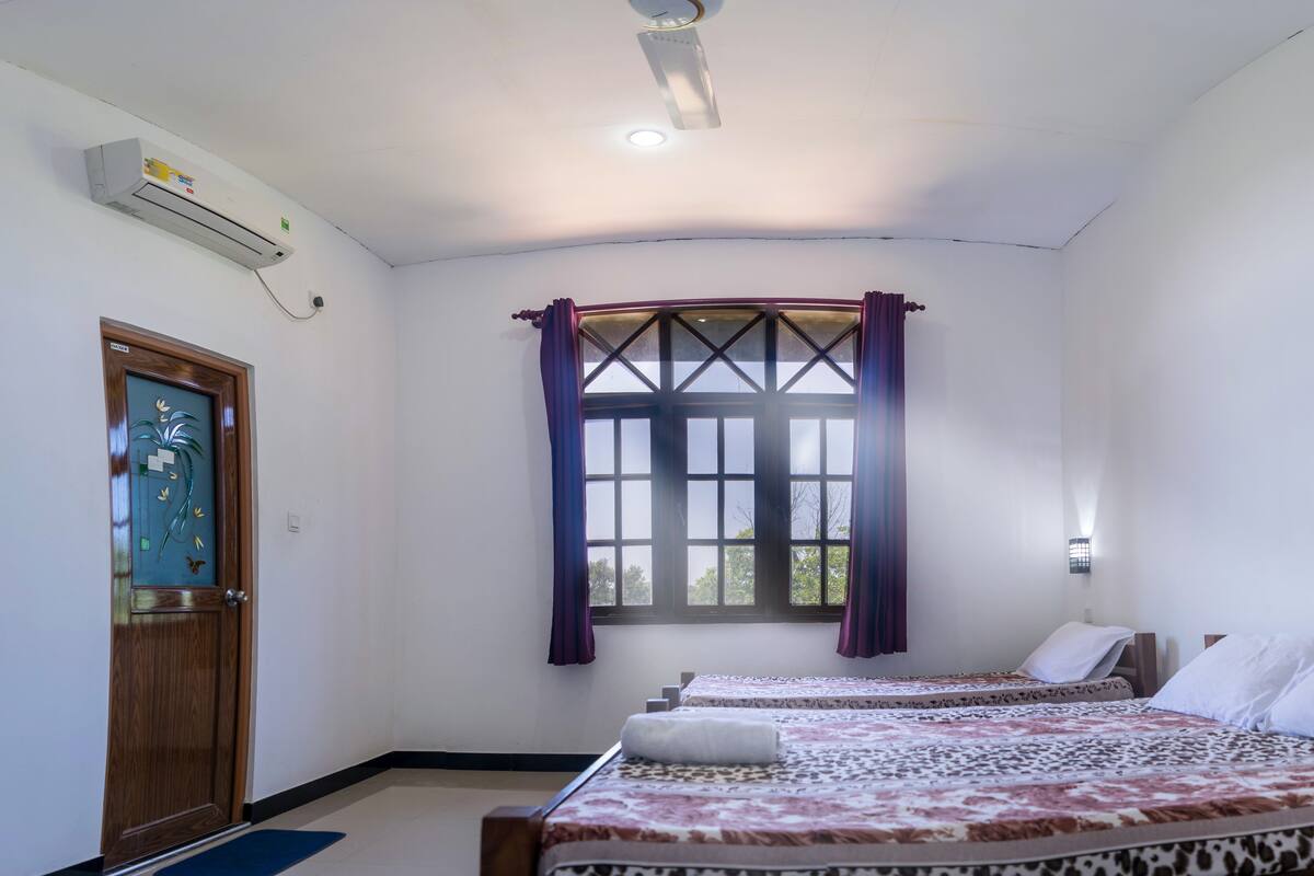Een hotelkamer met twee bedden, een raam met gordijnen, een airconditioning en een wandlamp.
