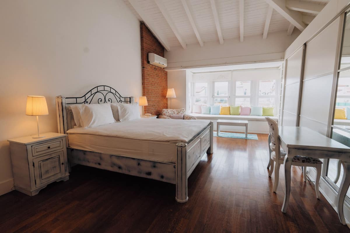 A bedroom with a bed, bedside tables, a desk, and a window with a view.