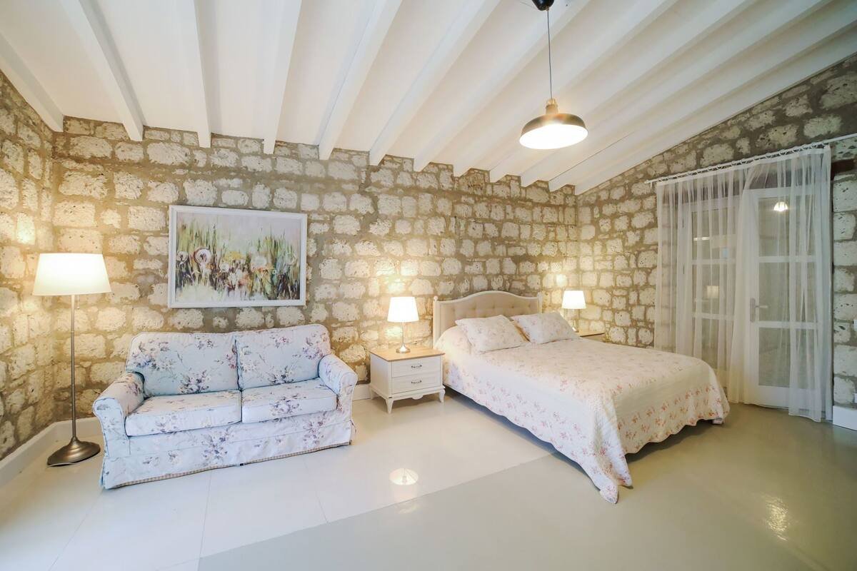 A bedroom with a stone wall, a bed, a sofa, and a painting.
