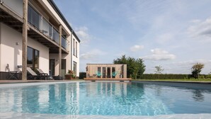 Un área de piscina moderna con una pileta transparente, sillas de descanso y una terraza de madera.