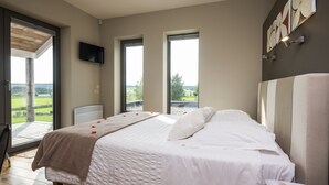 Un dormitorio con una cama grande, un televisor montado en la pared y vistas al exterior a través de una puerta corredera.