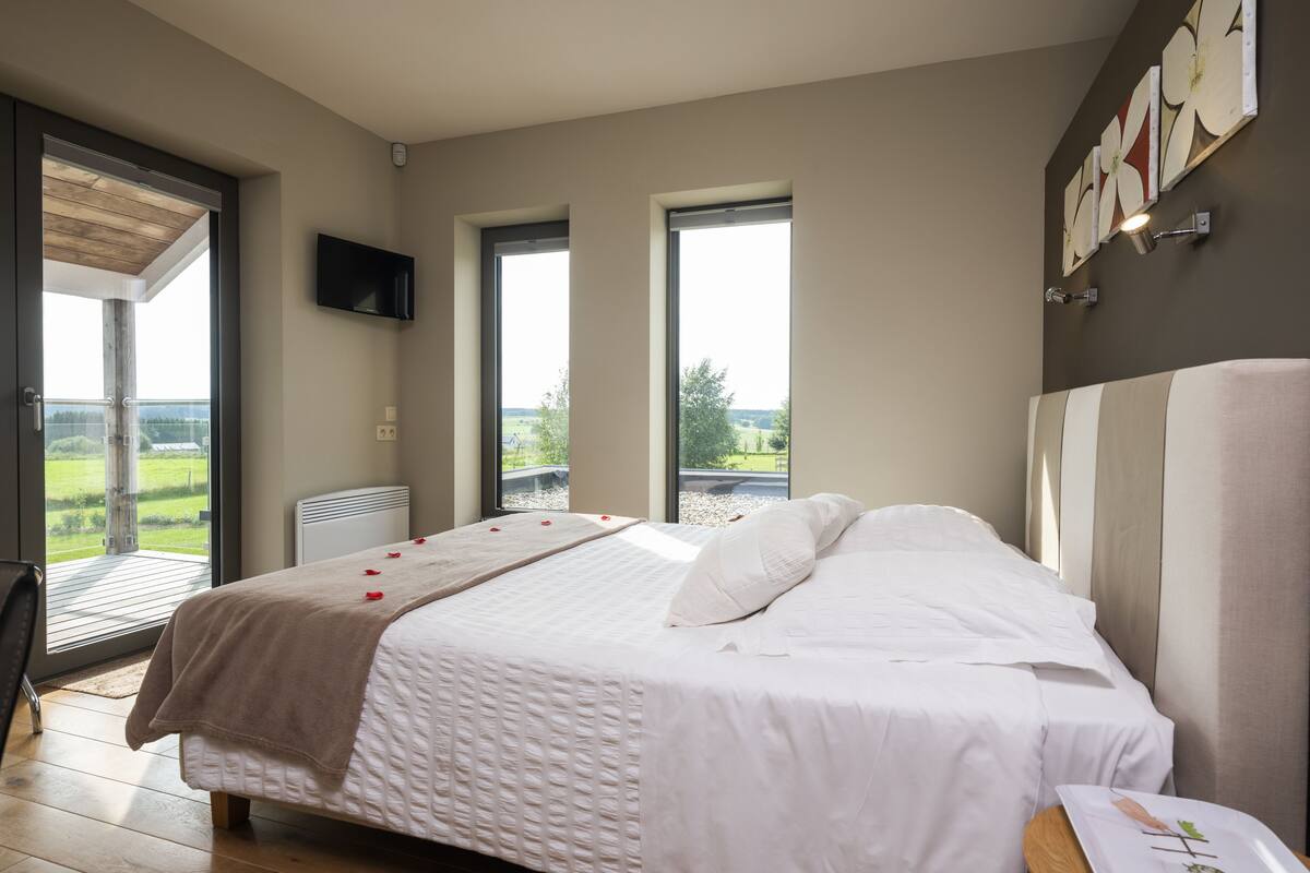 Een slaapkamer met een groot bed, een aan de muur bevestigde televisie en uitzicht op de omgeving door een schuifdeur.