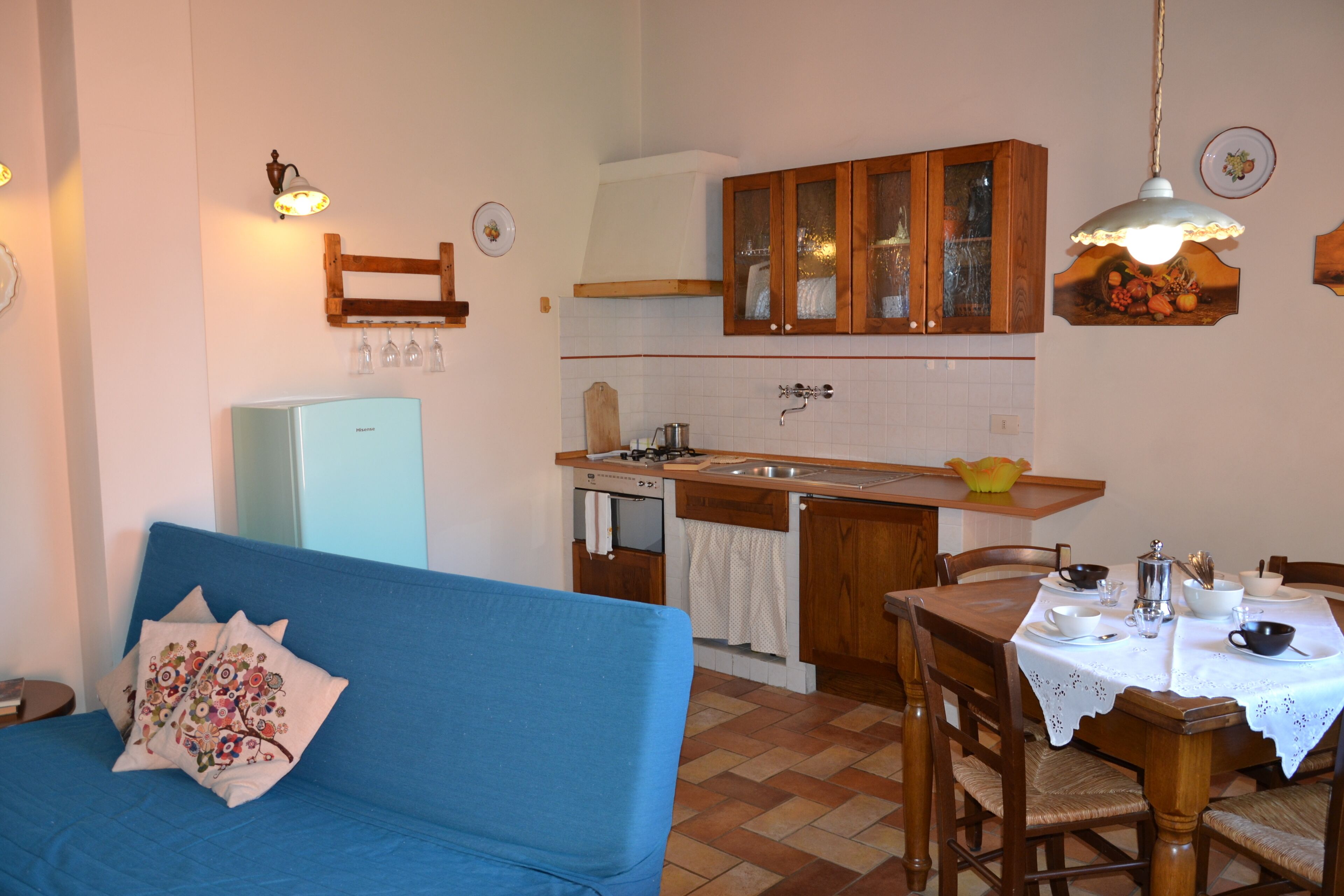 A cozy kitchen with a blue sofa, wooden cabinets, and a dining table set for four.