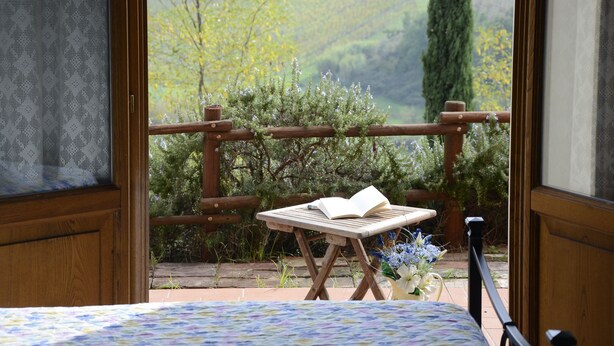 A balcony with a wooden table, an open book, and a view of a vineyard. - Agriturismo Corte in Poggio (Cerreto Guidi)