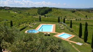 A pool area with two pools, surrounded by well-maintained lawns and trees, set against a backdrop of rolling hills and vineyards. - Agriturismo Corte in Poggio (Cerreto Guidi)