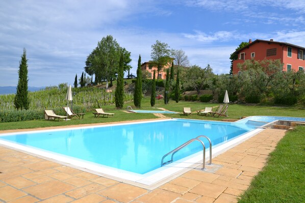 A swimming pool with lounge chairs and a red building in the background. - Agriturismo Corte in Poggio (Cerreto Guidi)