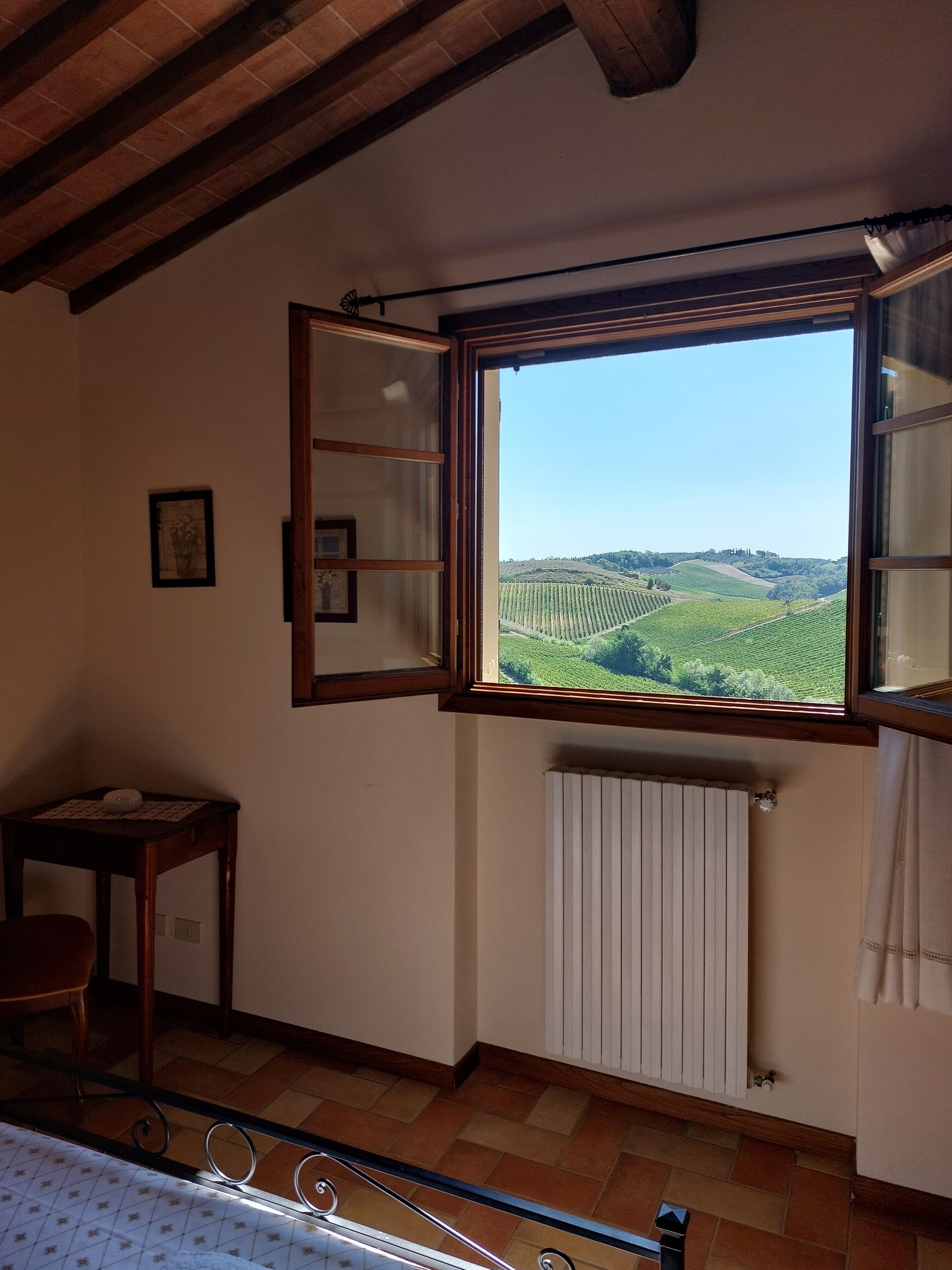 Une pièce dotée d’une grande fenêtre donnant sur un vignoble. On y trouve un radiateur sous la fenêtre, ainsi qu’une petite table et une chaise.