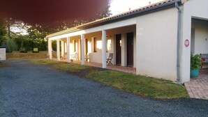 A single-story building with a covered patio area, a gravel driveway, and a small garden with potted plants.