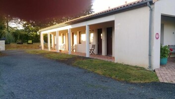 Un bâtiment d’un seul étage doté d’un patio couvert, d’une allée en gravier et d’un petit jardin agrémenté de plantes en pot.