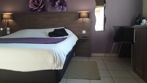 A hotel room with a bed, two wall-mounted lamps, a desk with a chair, and artwork on the wall.