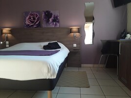 Une chambre d’hôtel comprenant un lit, deux lampes fixées au mur, un bureau avec une chaise et des œuvres d’art accrochées au mur.