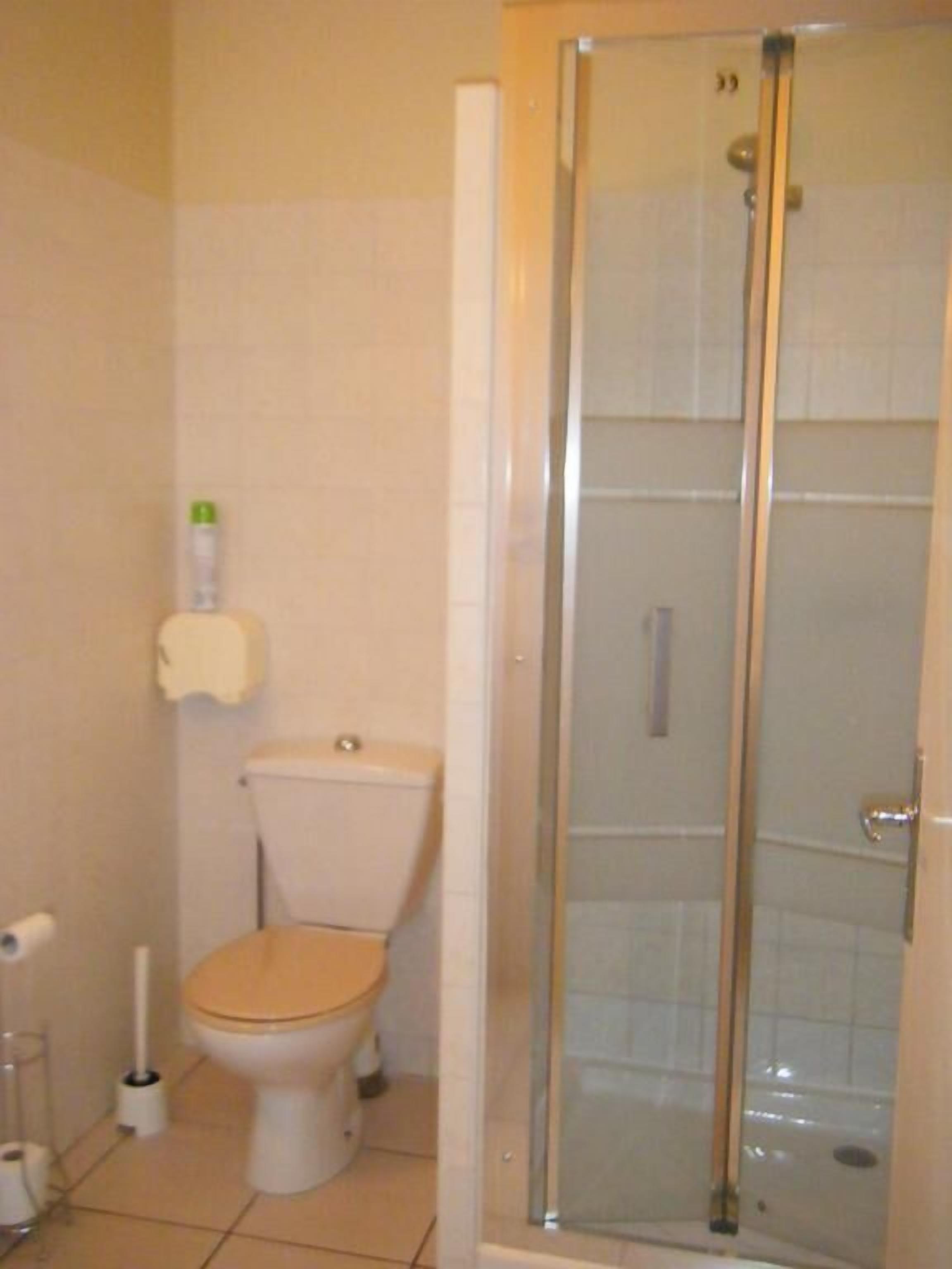 A bathroom with a toilet, a shower enclosure, and a toilet paper holder.