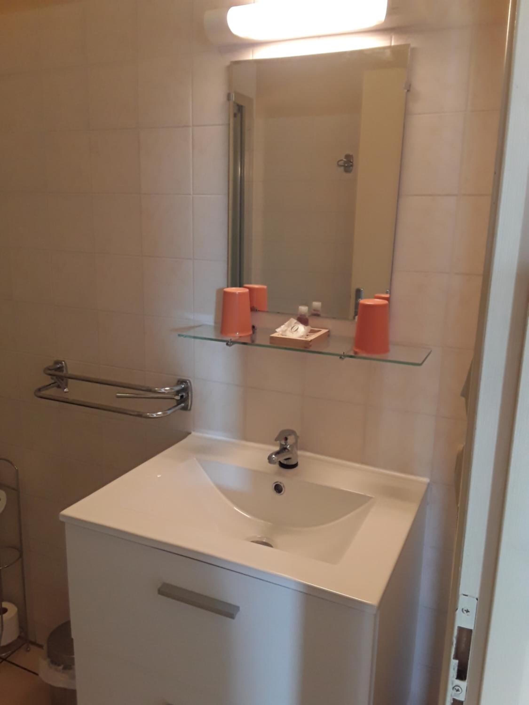 A bathroom with a white sink, a mirror, and orange soap dispensers on a shelf.