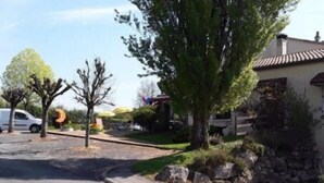 A residential street with a white car parked on the side, a tree-lined driveway, and a house with a tiled roof.