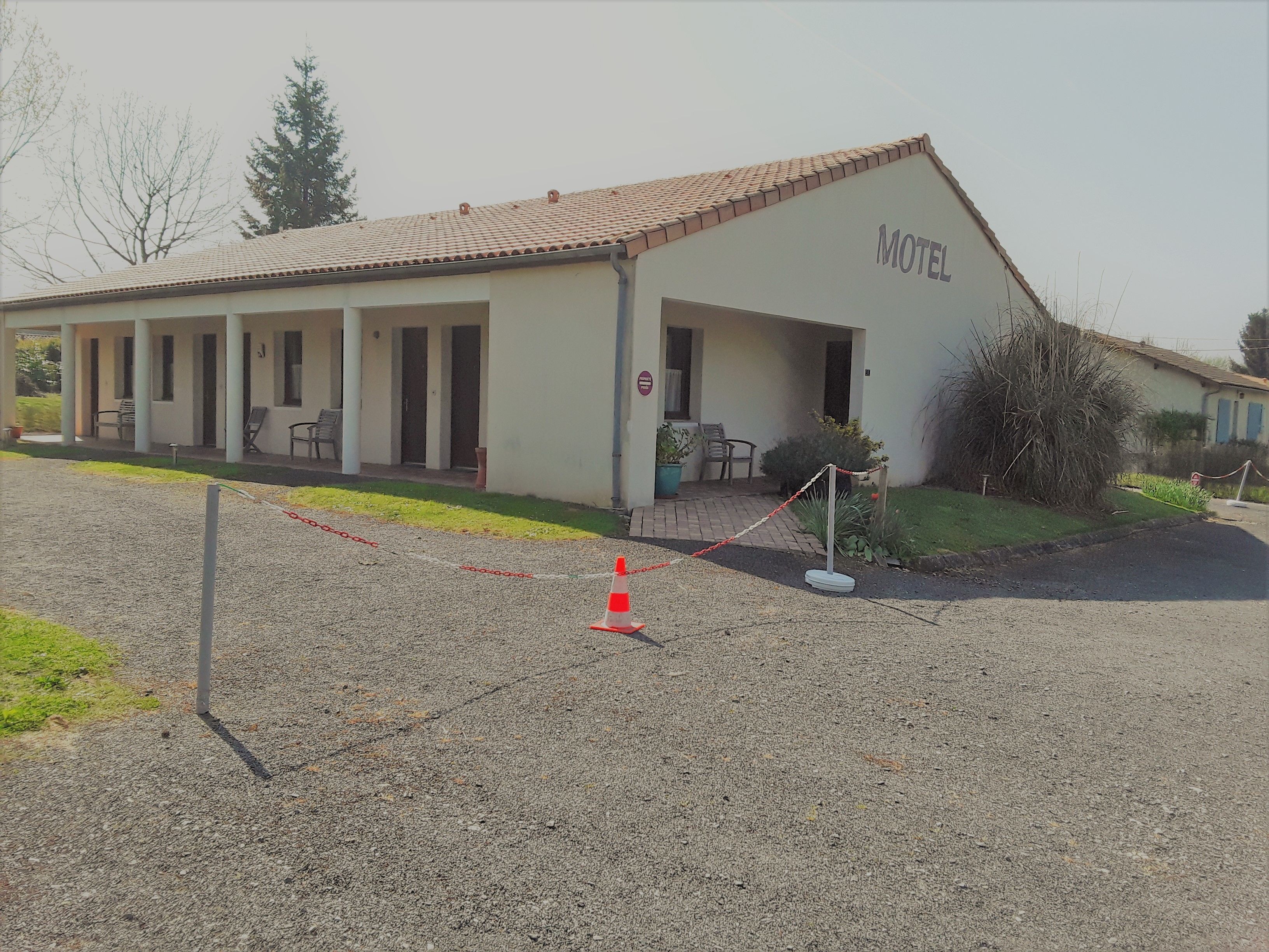 A motel with a tiled roof, a covered porch with chairs, and a sign indicating the name.