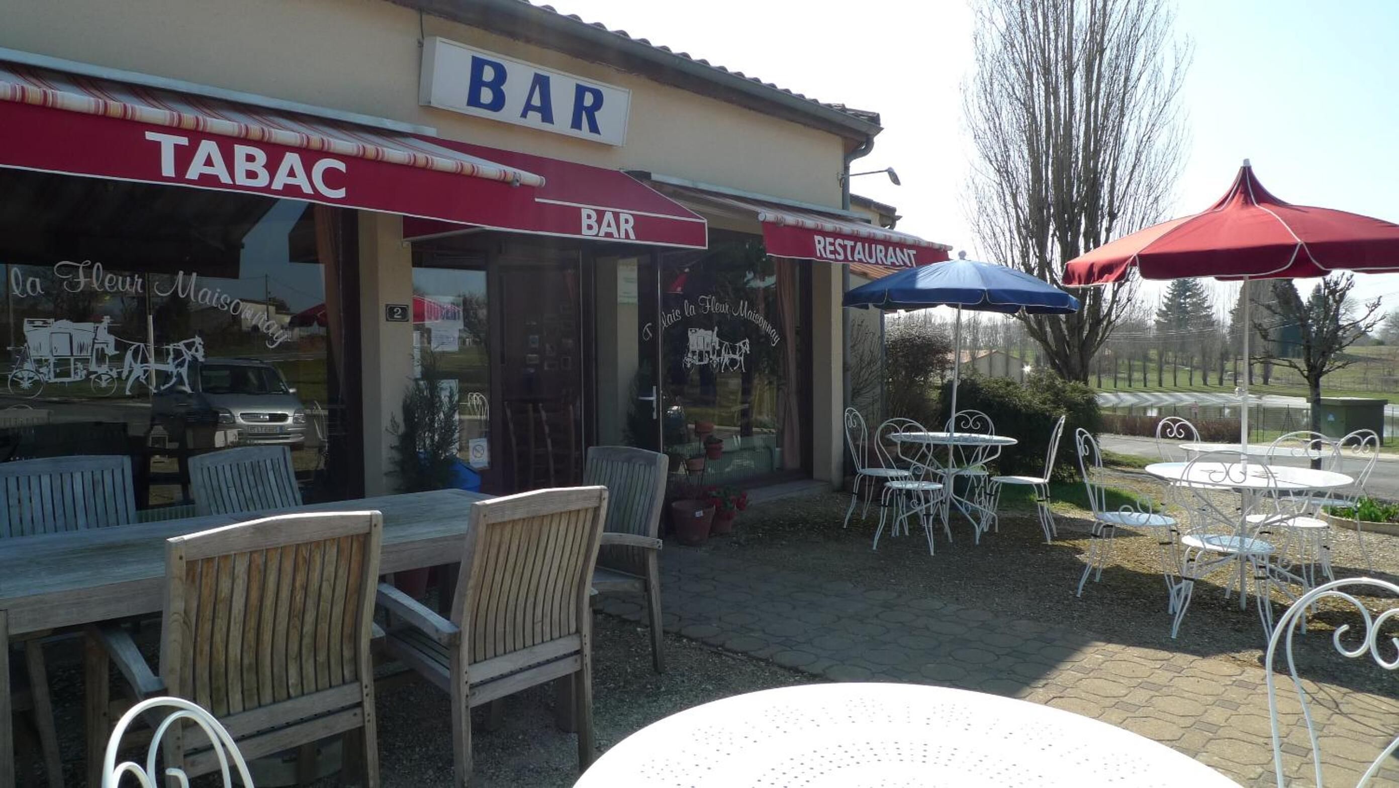 An outdoor seating area with wooden chairs and tables, a bar sign, and umbrellas.
