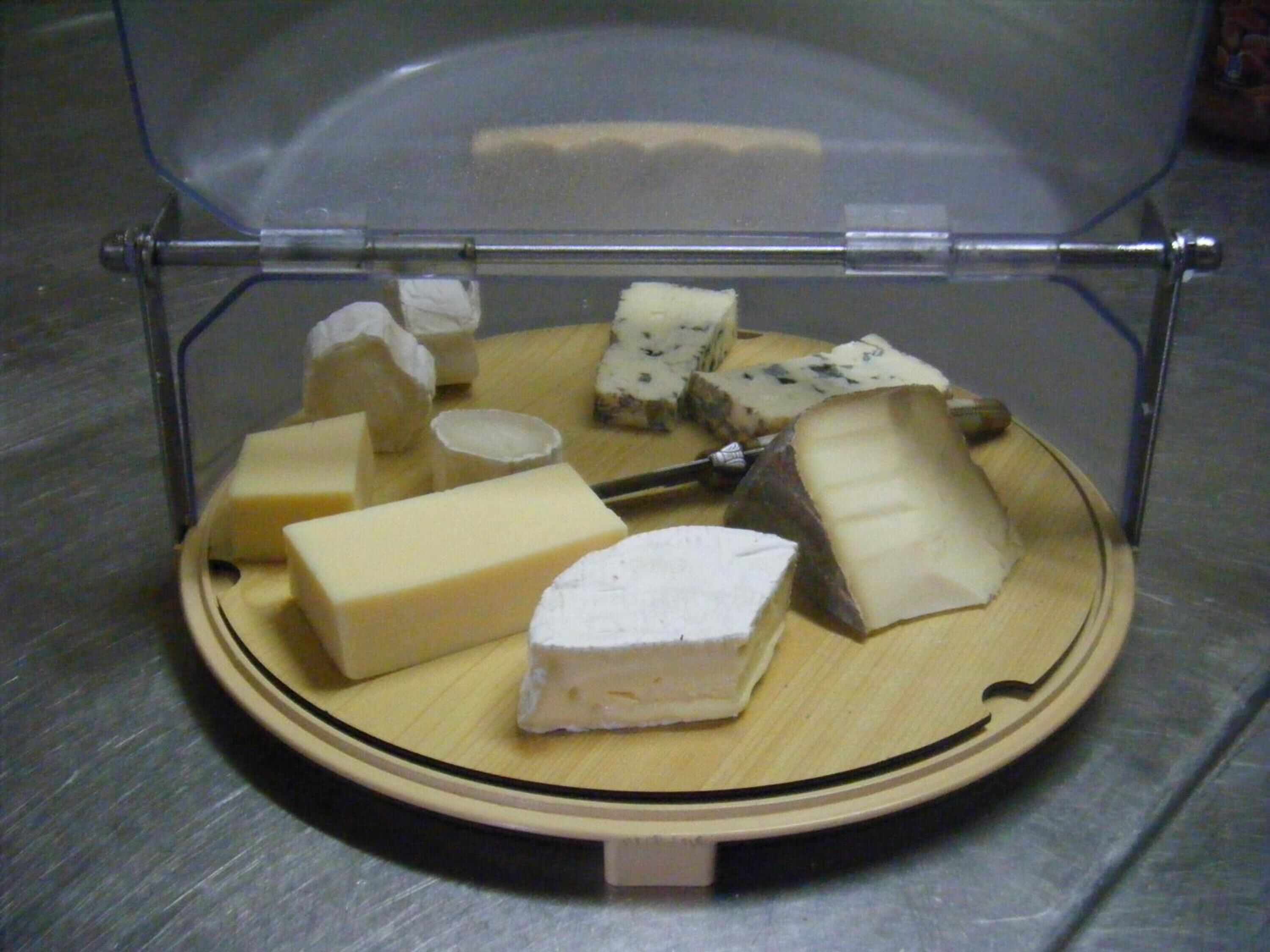 A variety of cheeses displayed on a wooden board inside a transparent case.
