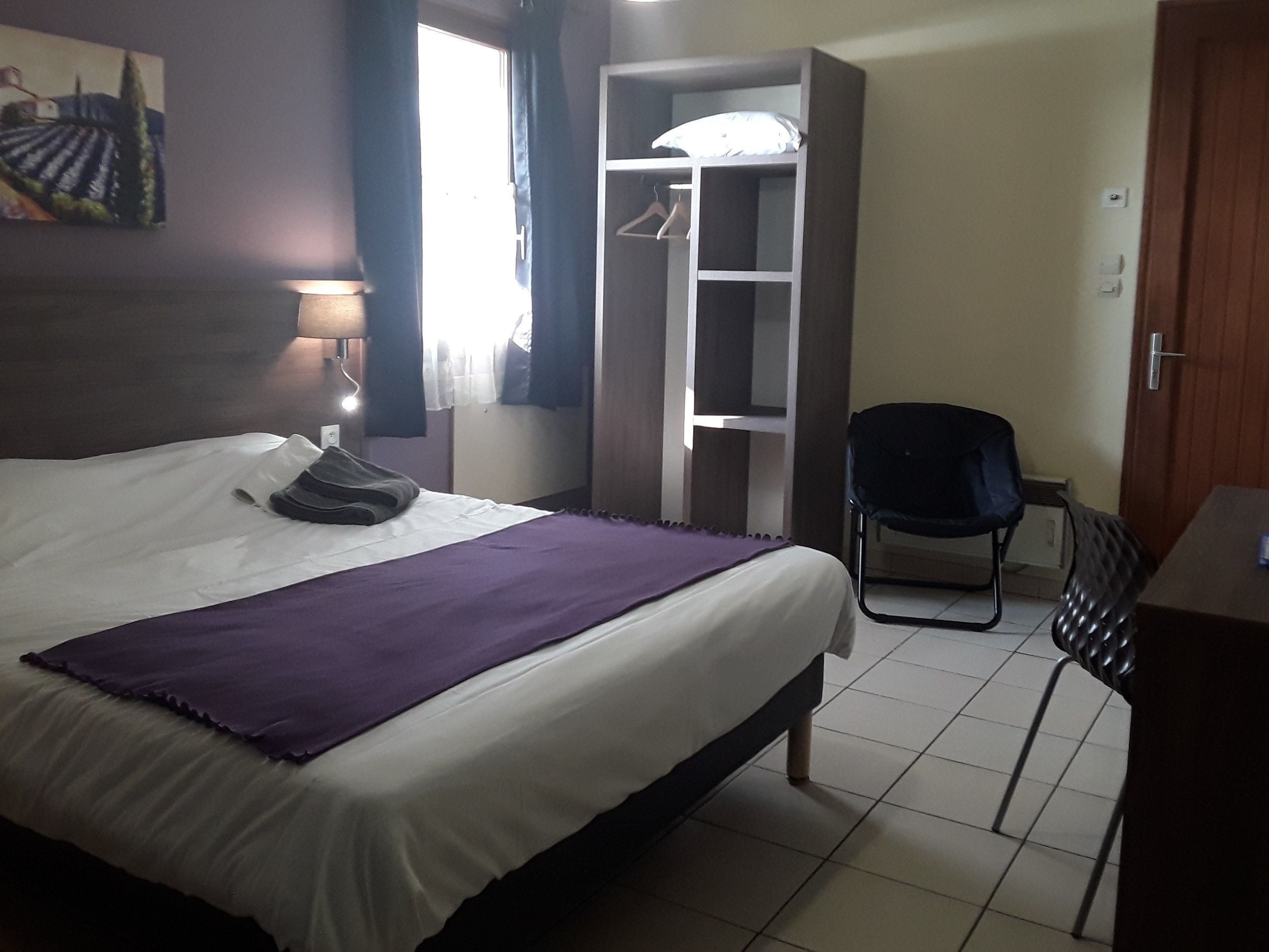Une chambre d’hôtel avec un lit, une chaise, une armoire et un tableau au mur.