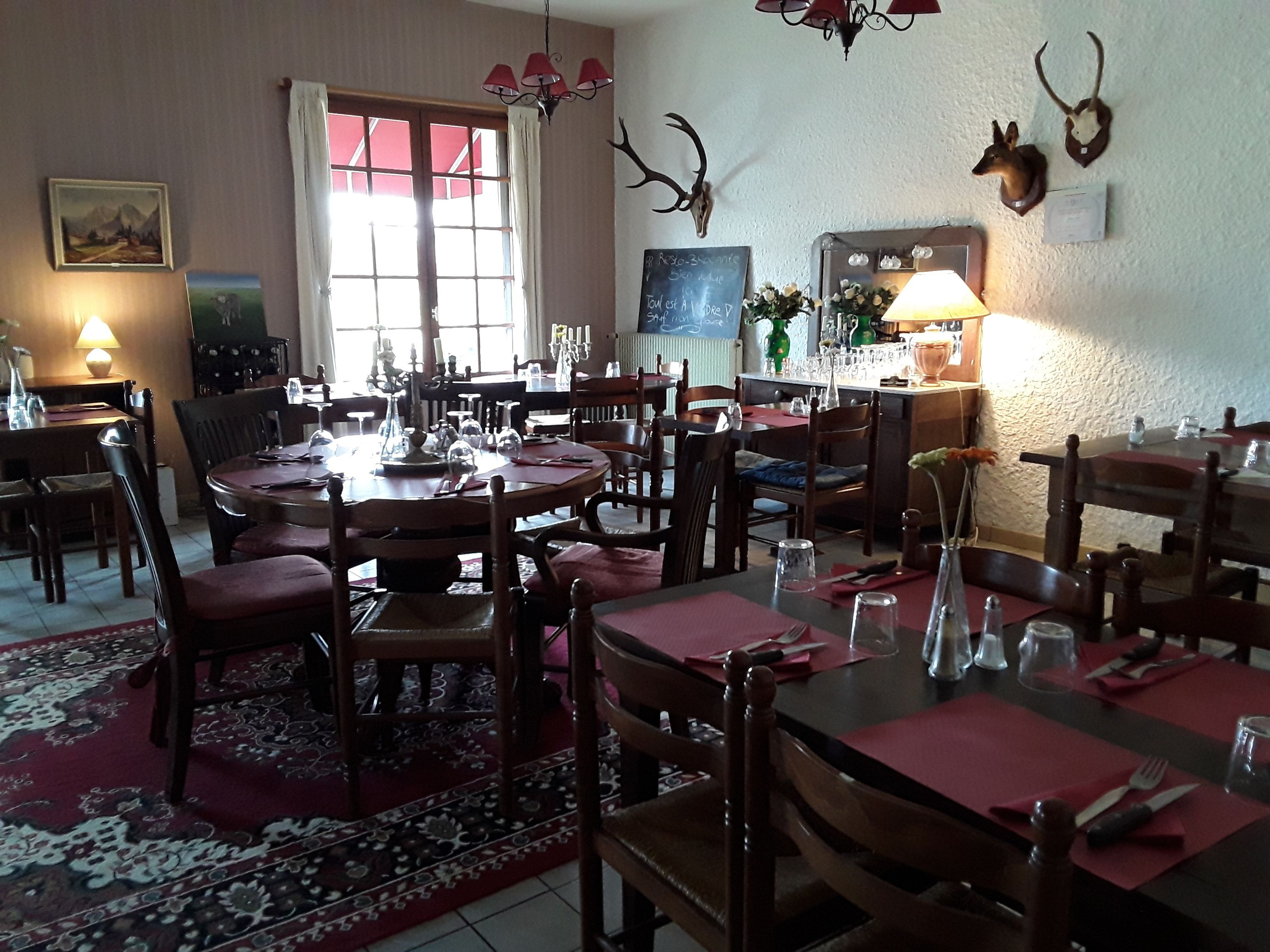 A dining area with multiple tables and chairs, a chandelier, and wall-mounted animal skulls.