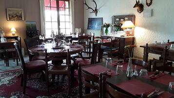 A dining area with multiple tables and chairs, a chandelier, and wall-mounted animal skulls.