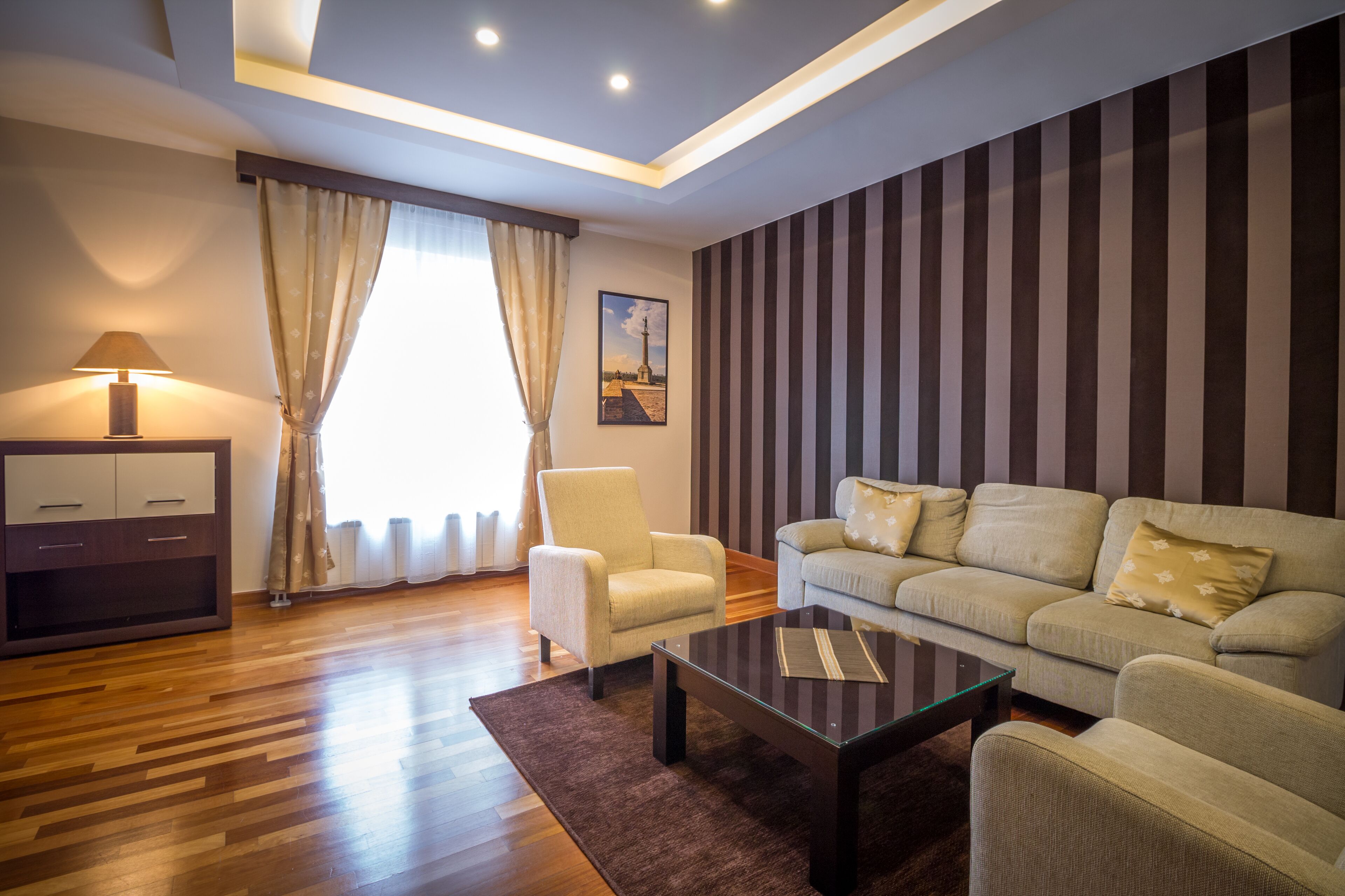 A modern living room with a sofa, armchairs, a coffee table, a lamp, and a painting on the wall.