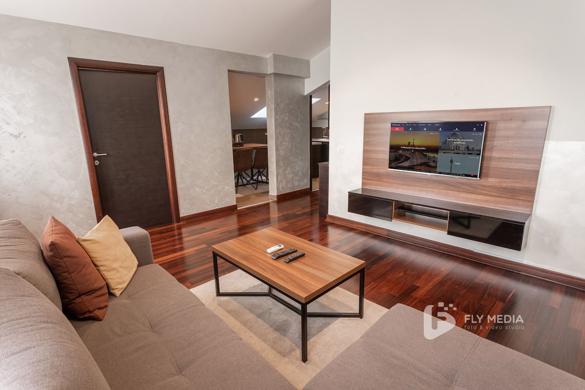 A modern living room with a sofa, coffee table, and a flat-screen TV mounted on the wall.