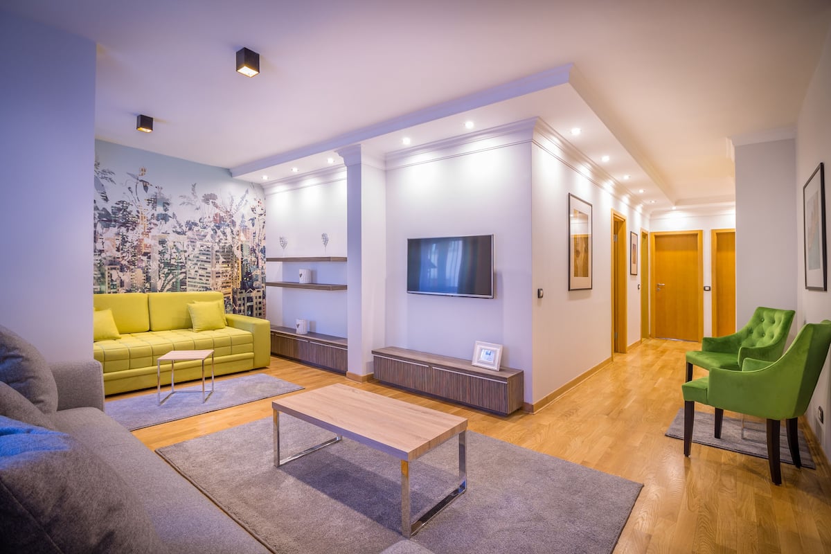 A modern living room with a yellow sofa, a grey sofa, a wooden coffee table, and a green armchair.