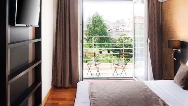 Un dormitorio con cama, televisor montado en la pared, balcón con sillas y equipo de aire acondicionado.