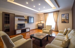 Ein modernes Wohnzimmer mit einer Couch, Sesseln, einem Couchtisch, einem Fernseher und einer Lampe.
