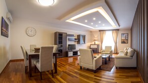 Una sala de estar moderna con piso de madera, un área de comedor con sillas, un sofá, un televisor y un reloj en la pared.
