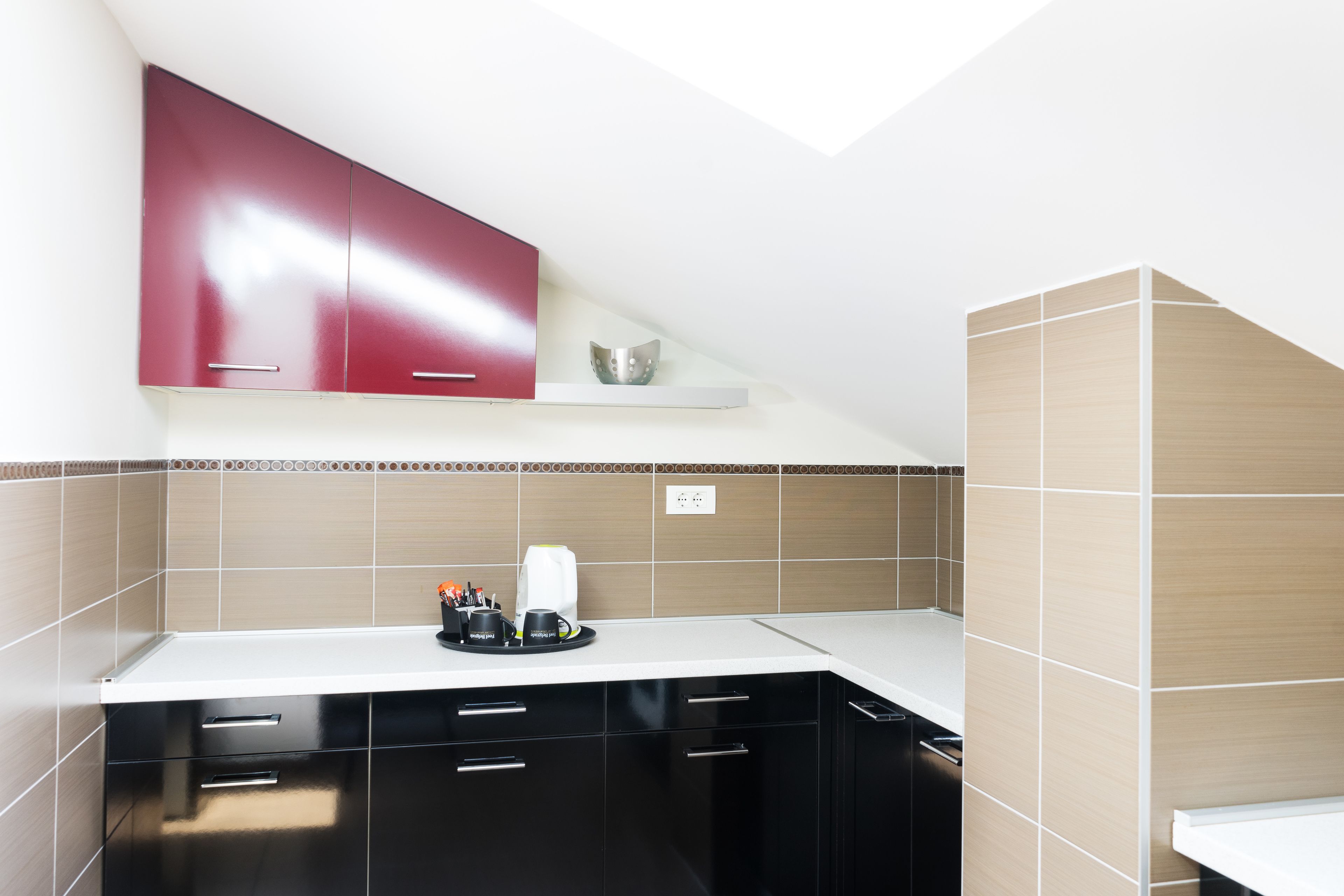 Una cocina moderna con armarios negros, encimera blanca y un mueble superior rojo.