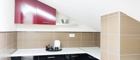 Una cocina moderna con armarios negros, encimera blanca y un mueble superior rojo.