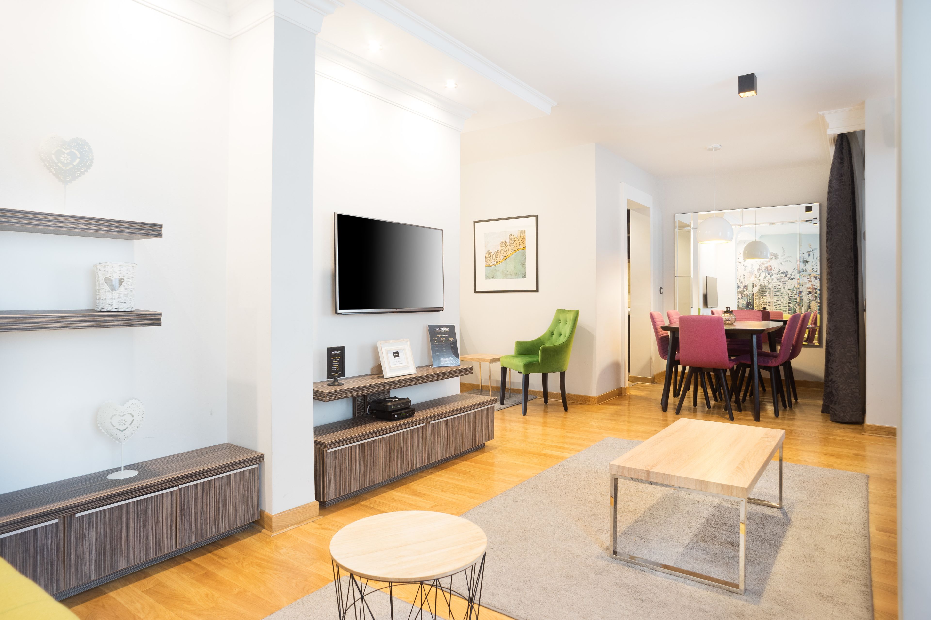 Un salon moderne avec un téléviseur à écran plat, un fauteuil vert, une table à manger avec des chaises et une table basse en bois.