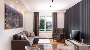 Una sala de estar moderna con un sofá seccional, una mesa de centro de vidrio, un televisor sobre un mueble de madera y un cuadro de gran formato con una vista urbana en la pared.